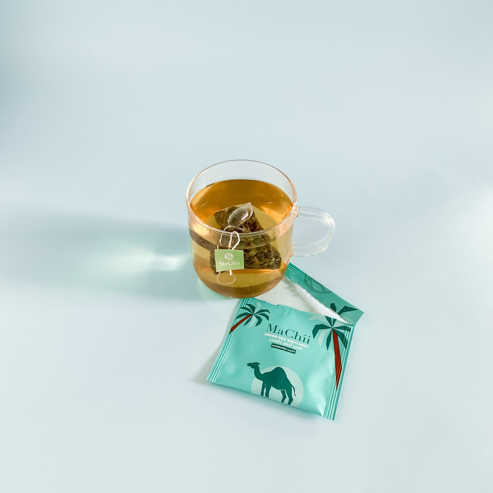 organic green tea with mint brewing in a glass cup. the tea bag is falling off the cup on the side. the wrapper is on the side of the picture on a wooden table