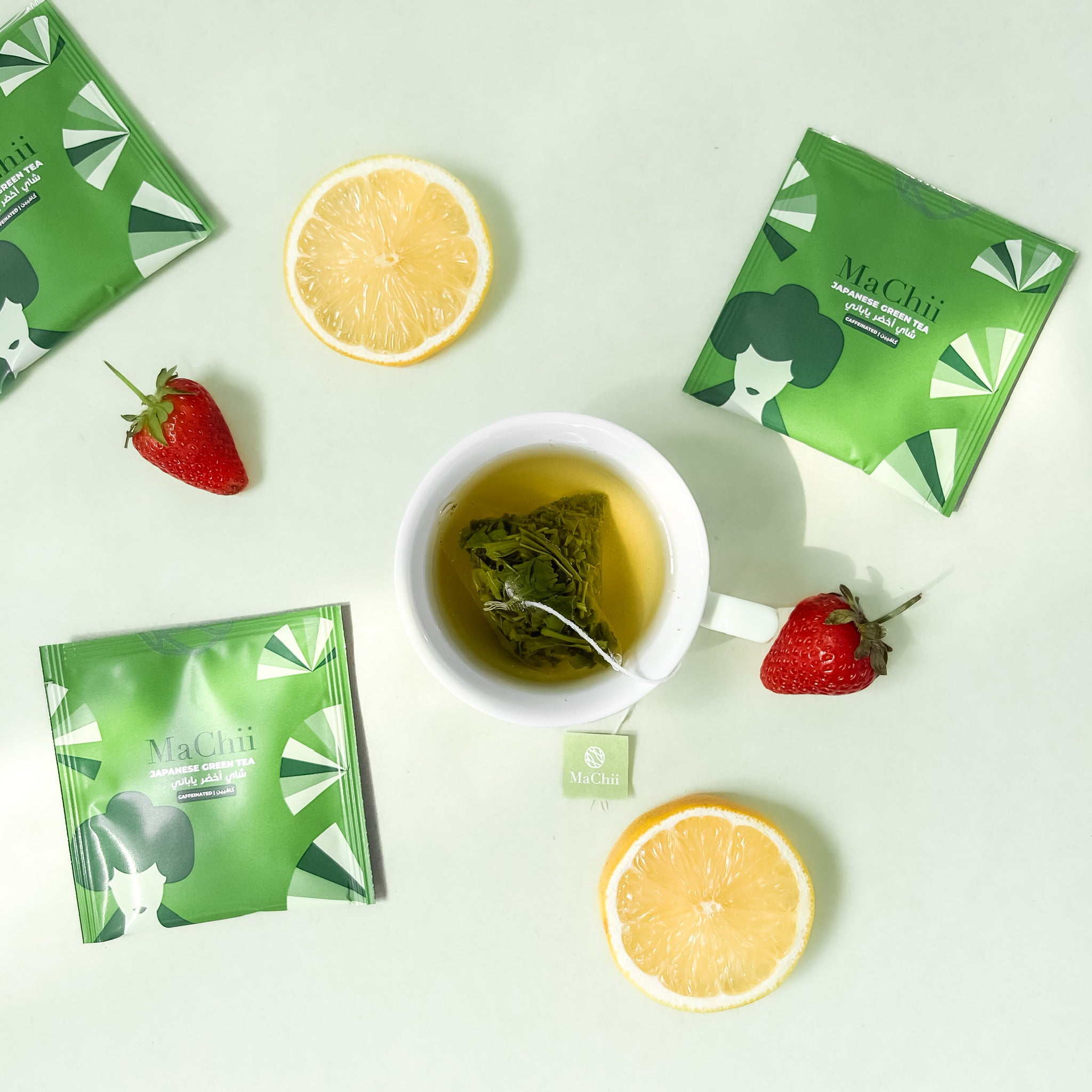 Japanese sencha green tea brewing in a white cup with 3 envelopes on the side and lemon and starwberries as decoration on the side