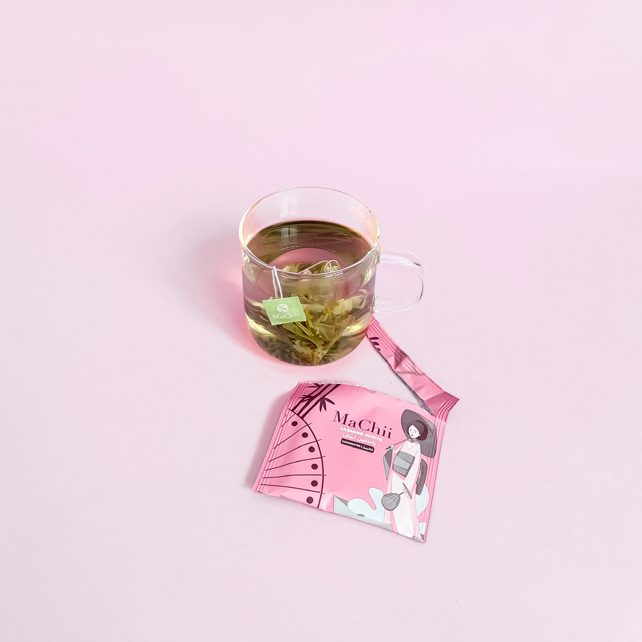 organic white tea with jasmine brewing in a mug. the tea is in a pyramid tea bag with the machii tea logo tag. the envelope packaging is wrapped open. 