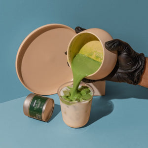 
                  
                    matcha latte being poured into milk. silver matcha tin in the background
                  
                