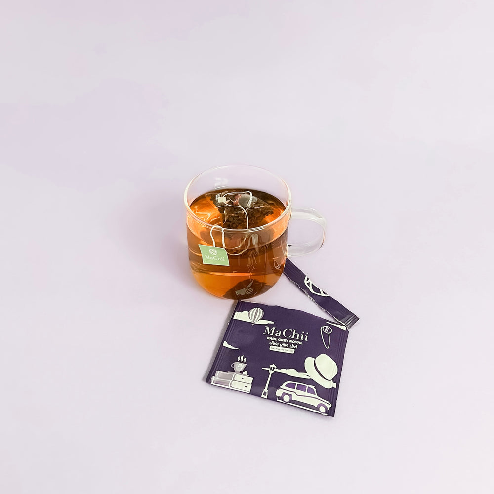organic earl grey tea brewing in a glass cup. the tea tag is falling off the side and the packaging is wrapped open on the side, 