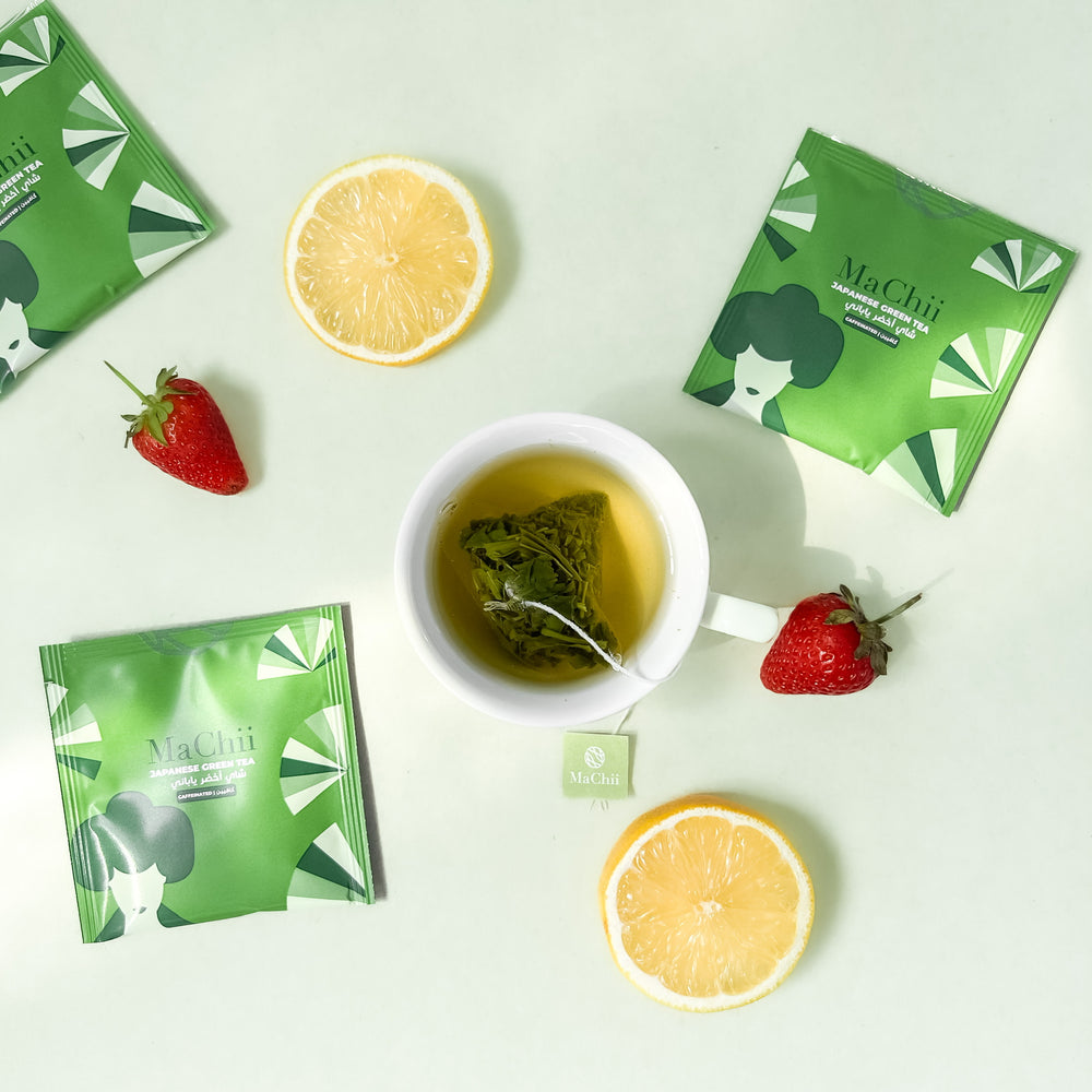 
                  
                    Japanese sencha green tea brewing in a white cup with 3 envelopes on the side and lemon and starwberries as decoration on the side
                  
                