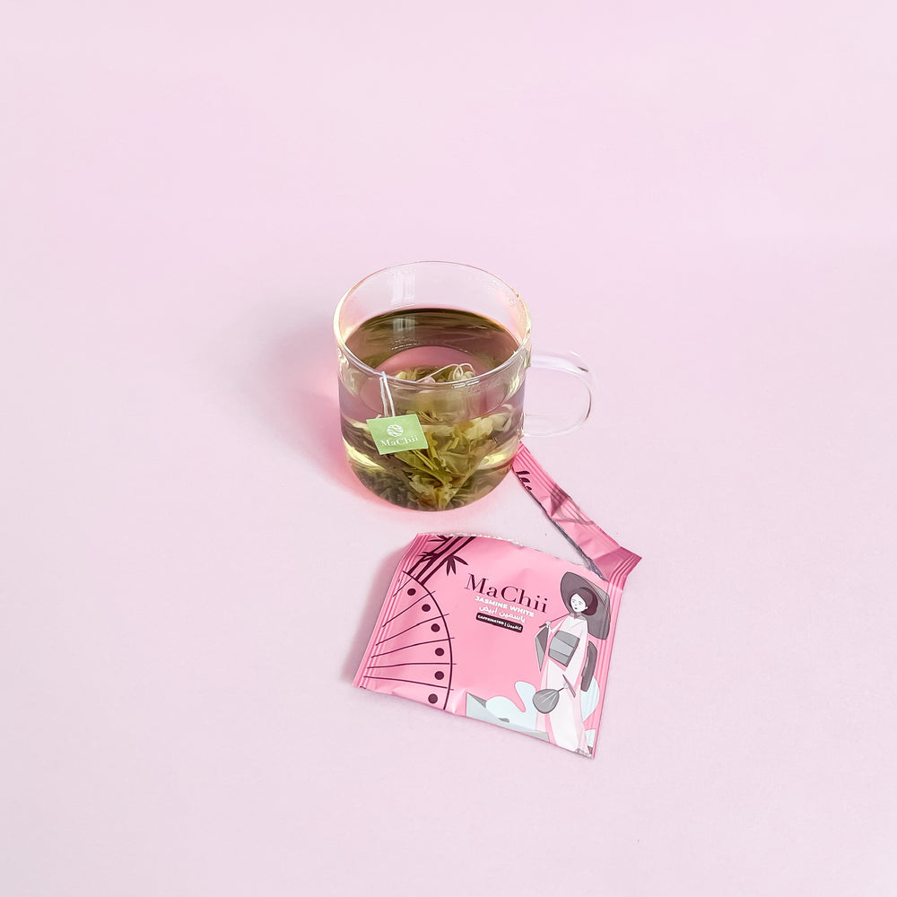 
                  
                    organic white tea with jasmine brewing in a mug. the tea is in a pyramid tea bag with the machii tea logo tag. the envelope packaging is wrapped open. 
                  
                