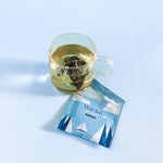 Organic milk oolong tea in a that is brewing in a cup. Enevlope teared open on the table next to the tea cup.