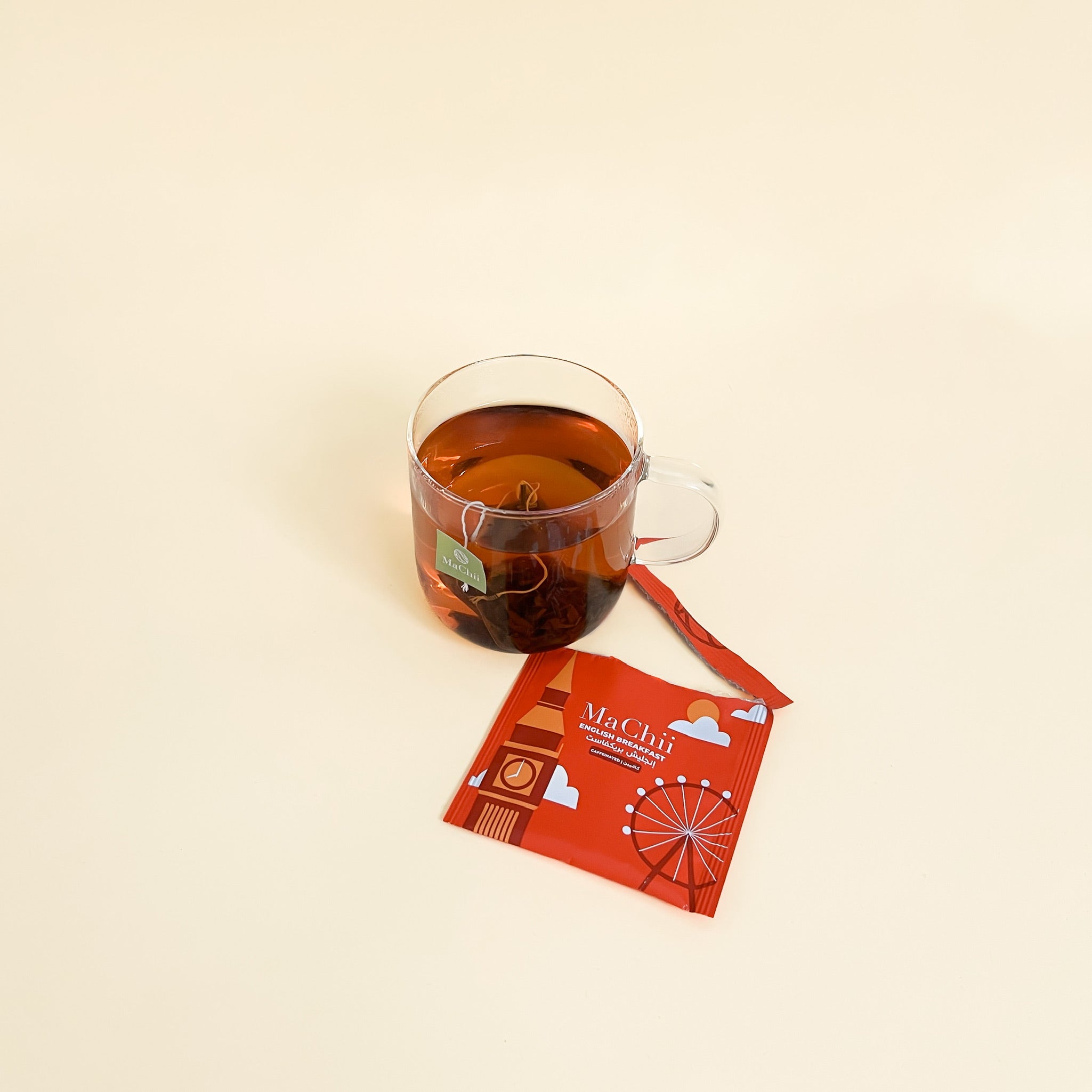 organic English breakfast tea bag infusing in hot water. a torn tea envelope on the side next to the cup. tea tag sticking out of cup